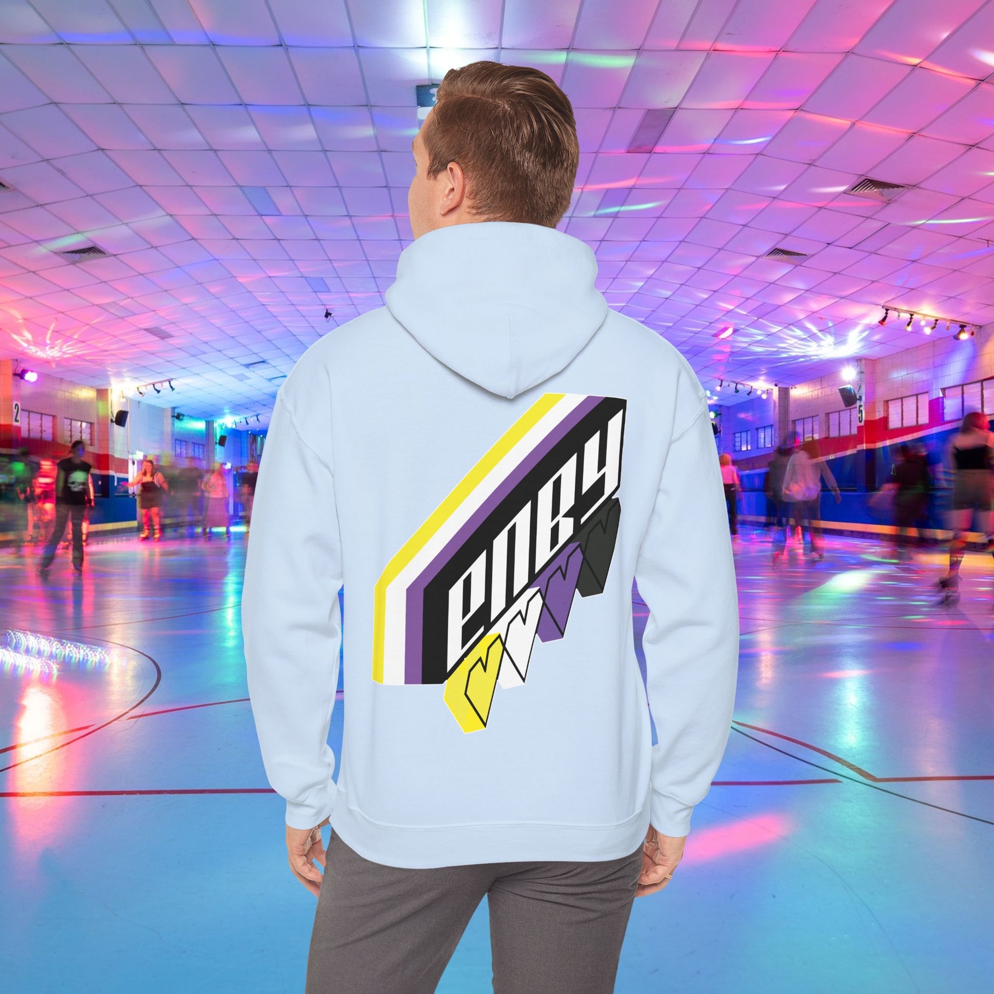 A person wearing the high-quality Printify ENBY Heart Hoodie, a unisex heavy blend hooded sweatshirt, with its colorful geometric nonbinary flag designs on the back, stands in a retro-style roller skating rink. The background features neon lights, blurred skaters, and a vibrant atmosphere.