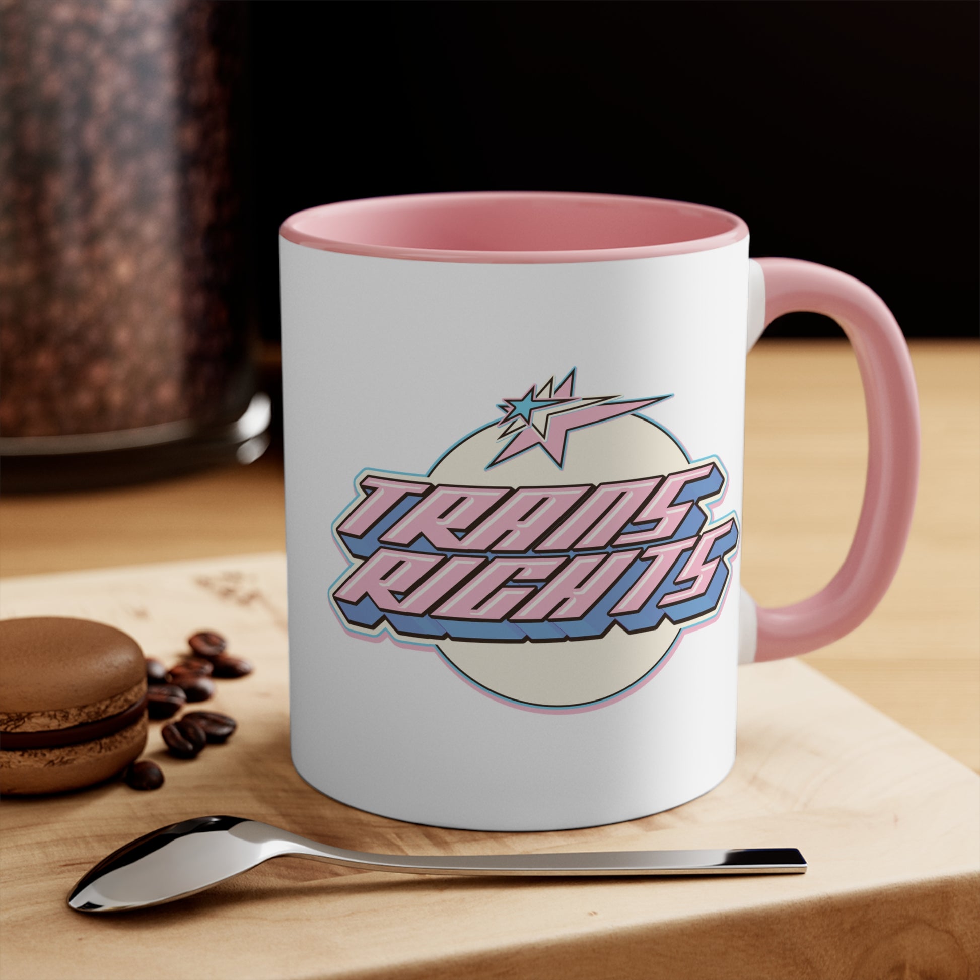 The Trans Rights colorful accent mug by Printify showcases a white coffee mug with a pink handle and vibrant interior, featuring the bold, retro-style text "TRANS RIGHTS" against a circular, off-white background. Above the text is a stylized star with dynamic lines that reflect the colors of the transgender pride flag, creating an energetic sense of movement.