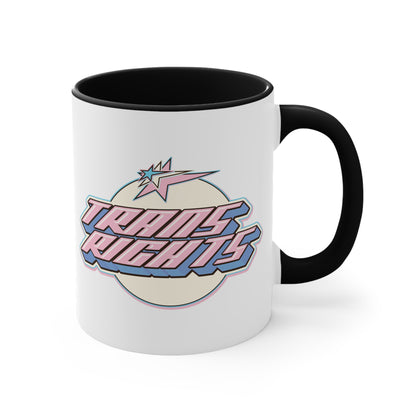 The Trans Rights colorful accent mug by Printify showcases a white coffee mug with a pink handle and vibrant interior, featuring the bold, retro-style text "TRANS RIGHTS" against a circular, off-white background. Above the text is a stylized star with dynamic lines that reflect the colors of the transgender pride flag, creating an energetic sense of movement.