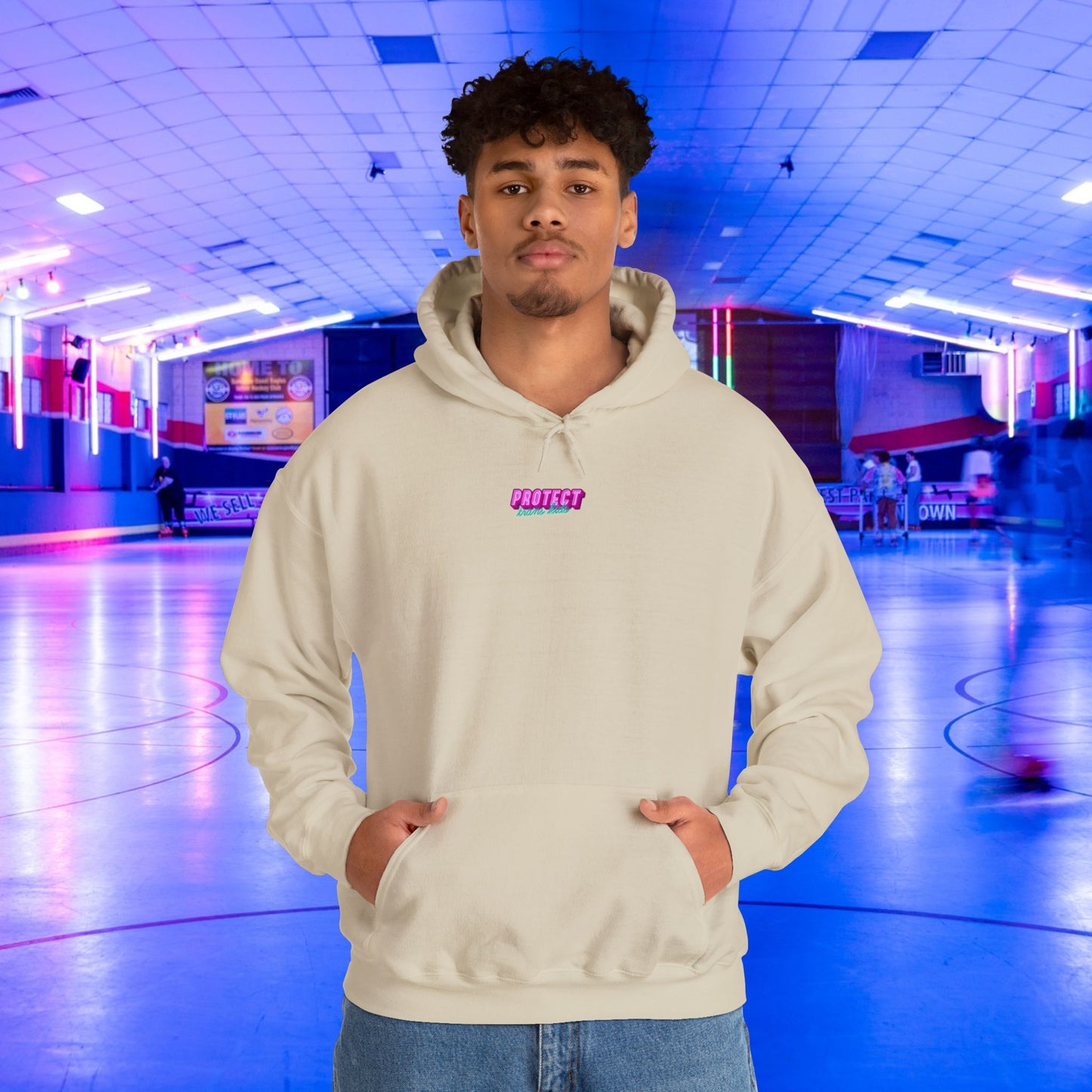 In an indoor skating rink, a person sports the "Protect Trans Kids Hoodie - Australian Shipping," made from ethically grown cotton. The background features a colorful blue and purple glow with a smooth floor and motion-blurred figures skating around.