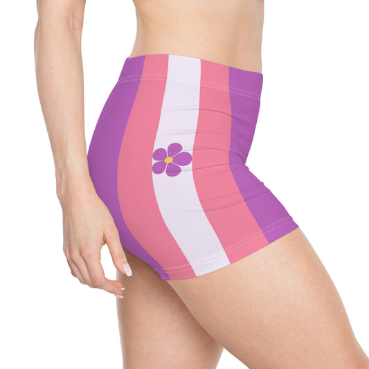 A person's lower torso and legs are shown, wearing Printify's Sapphic Pride Flag Short Shorts featuring vertical stripes in pink, white, and purple. The moisture-wicking fabric ensures comfort while a small purple flower with a yellow center adorns the side. The person’s hand rests confidently on their hip.