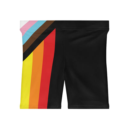 A person is wearing Progress Pride Bike Shorts by Printify, which feature a colorful design with a rainbow pride flag incorporating stripes for people of color and the transgender community. These moisture-wicking shorts fit closely to the body.