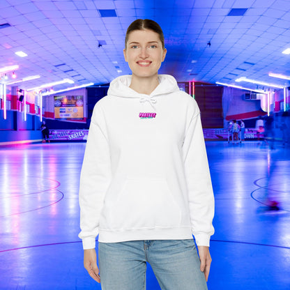 Wearing a "Protect Trans Kids Hoodie - Australian Shipping," crafted from ethically grown cotton, and jeans, a smiling person stands inside a vibrant roller skating rink with neon lights and a blue floor. Skaters whirl in the background, adding to the lively atmosphere.