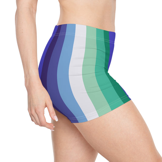 A person wearing the Printify Gay Men Pride Flag Short Shorts, high-waisted unisex active wear shorts featuring vibrant vertical stripes in various shades of blue, green, and white. The person's waist and upper thigh are visible, showcasing the comfortable fit and striking design of the shorts.