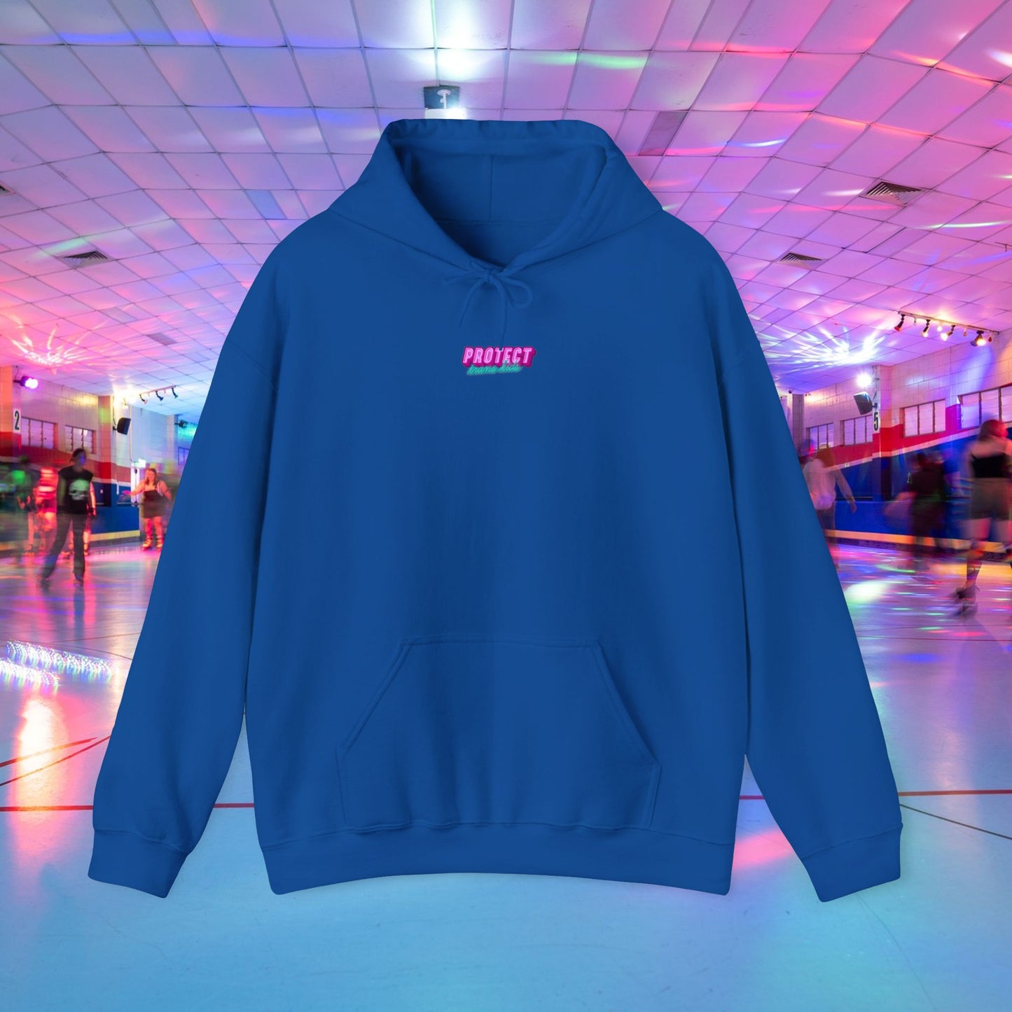 Displayed is the "Protect Trans Kids" unisex heavy blend hoodie, featuring "PROTECT" in pink across the chest. Made from ethically grown cotton, it stands out against a colorful roller skating rink backdrop with vibrant lights and skaters.