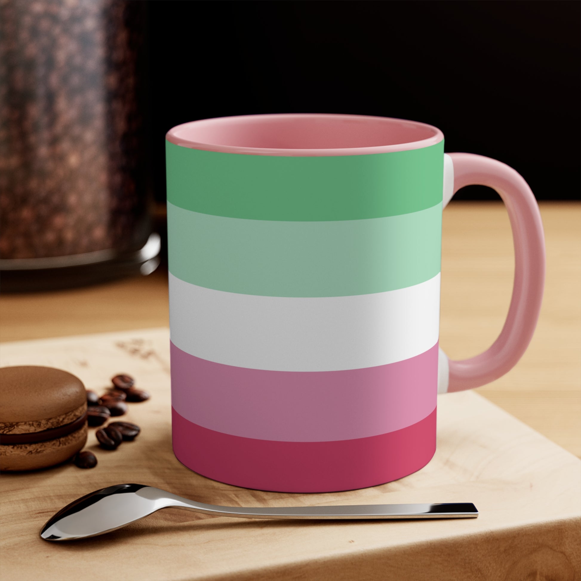 The Abro, Abroromantic, Abrosexual pride flag Accent Mug by Printify is a ceramic mug designed with horizontal stripes in green, light green, white, pink, and red to reflect the vibrant hues of the Abrosexual pride flag. It also features a pink handle and a colorful interior.