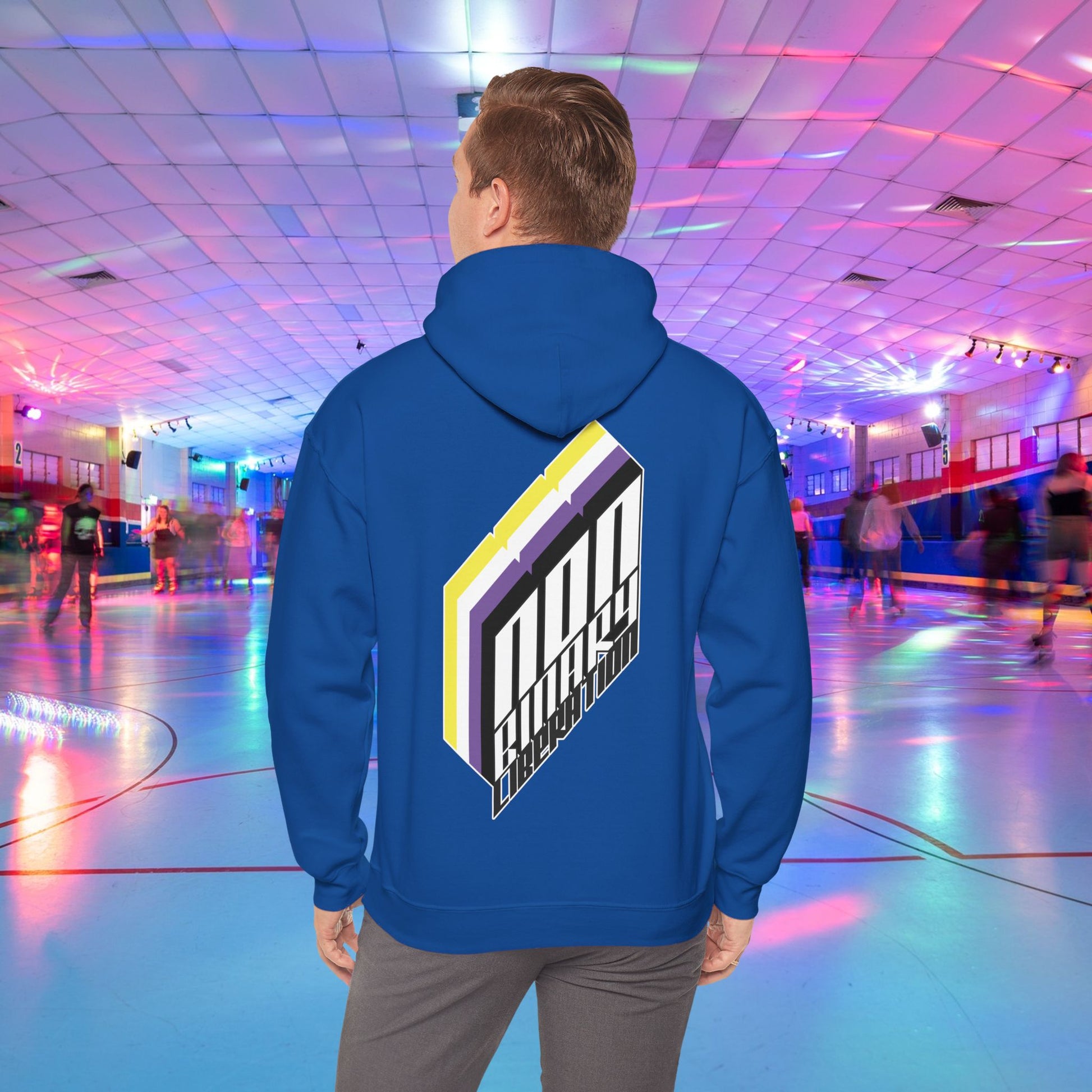 A person wearing the Non-Binary Liberation Hoodie - Australian Shipping by Printify, showcasing a vibrant geometric design on the back in nonbinary pride flag colours, stands in the middle of a roller skating rink. The rink is bathed in vibrant lights of various colors, with several people skating in the background.