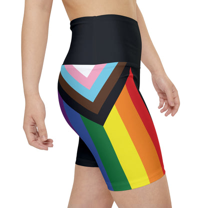 A person wearing Printify's Progress Pride Rainbow Flag High-Waisted Workout Pants, featuring a vibrant design perfect for an active lifestyle. The shorts display horizontal stripes in black, brown, light blue, pink, white, red, orange, yellow, green, and blue against a white background.