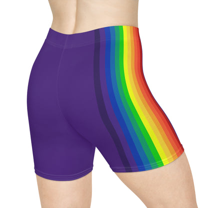 A person is wearing Rainbow and Purple Bike Shorts, which feature a bold, vertical rainbow pride flag stripe pattern on the side in red, orange, yellow, green, blue, and purple. These form-fitting shorts are made from moisture-wicking polyester spandex and have a neutral white background.