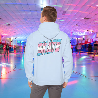 A man with light brown hair, wearing a black hoodie that features "SKATE" in large, colorful letters on the back, stands in a roller skating rink illuminated by vibrant lighting with people skating in the background. The high-quality SKATE Trans Flag Hoodie is made from ethically grown US cotton and is part of Printify's unisex heavy blend collection. Available for Australian shipping.