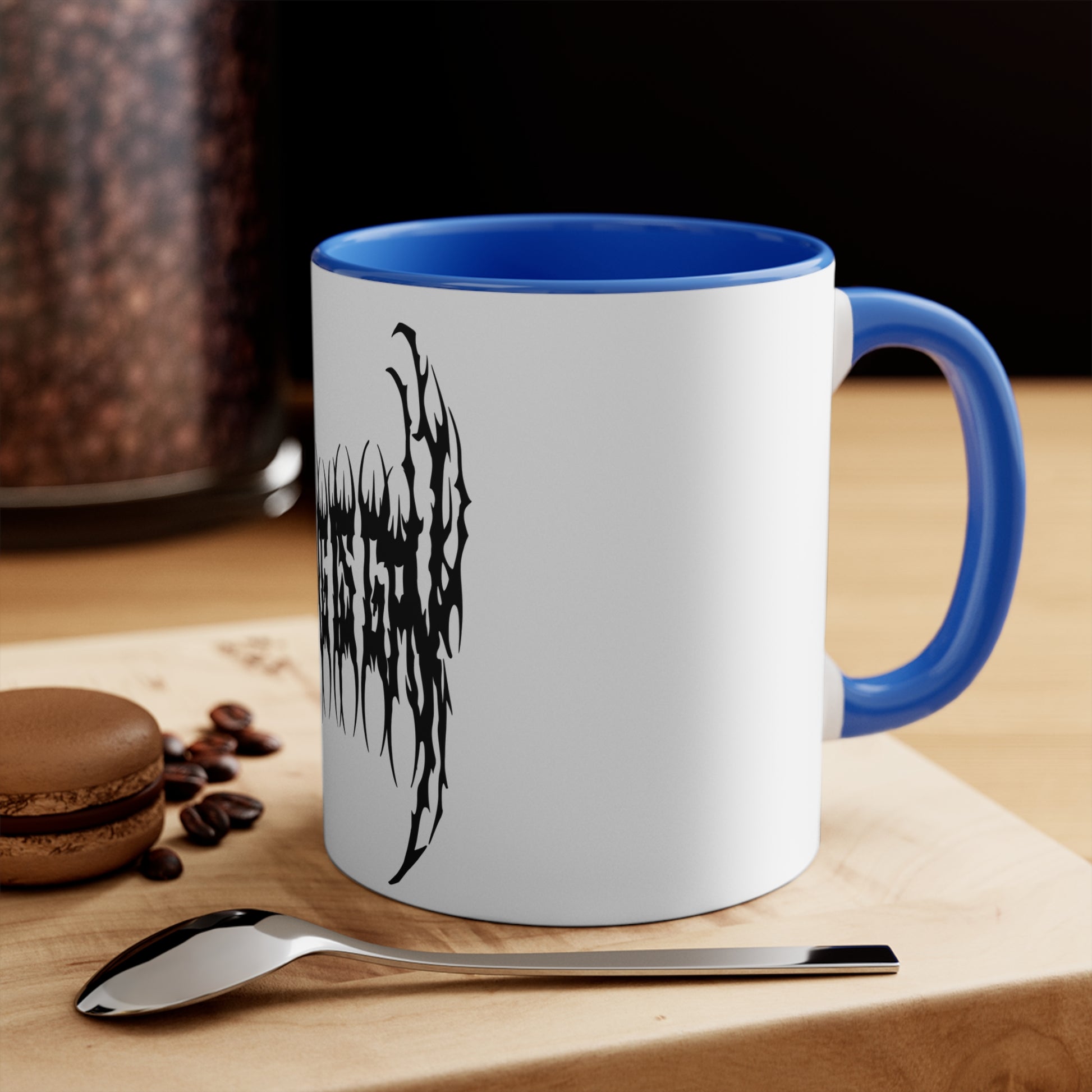 The "SKATING IS GAY but make it death metal accent mug" by Printify is a white mug with a black interior featuring an intricate design that resembles sharp, thorny text. Styled in a death metal font, the symmetrical design has an aggressive, edgy appearance that makes the text difficult to read due to its complex, spiky style.