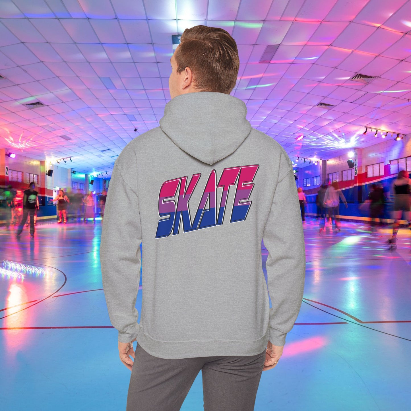 A person in a SKATE Bisexual Pride Hoodie from Printify, with bold and colorful "SKATE" lettering on the back, stands in a brightly lit roller skating rink. The background features skaters gliding on a shiny floor under a ceiling with vibrant, multicolored lights. This unisex heavy blend hooded sweatshirt showcases original designs and is available for Australian shipping.