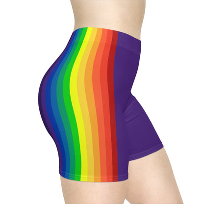 A person is wearing Rainbow and Purple Bike Shorts, which feature a bold, vertical rainbow pride flag stripe pattern on the side in red, orange, yellow, green, blue, and purple. These form-fitting shorts are made from moisture-wicking polyester spandex and have a neutral white background.