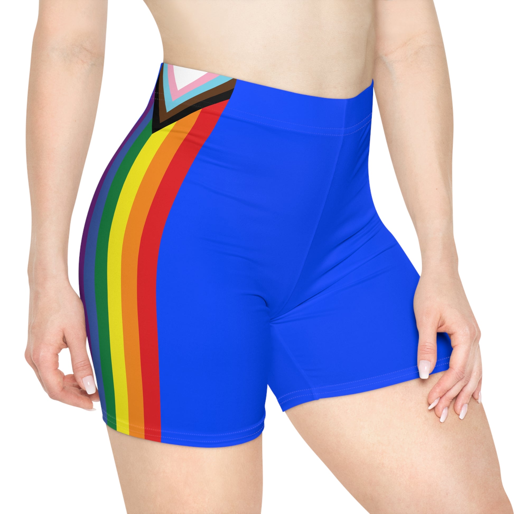 The image showcases a person from the side wearing Printify's Progress Pride Rainbow Flag and Blue Bike Shorts, which feature a vibrant rainbow design incorporating the Pride flag colors, transgender flag hues, and brown and black stripes at the top to symbolize inclusivity.