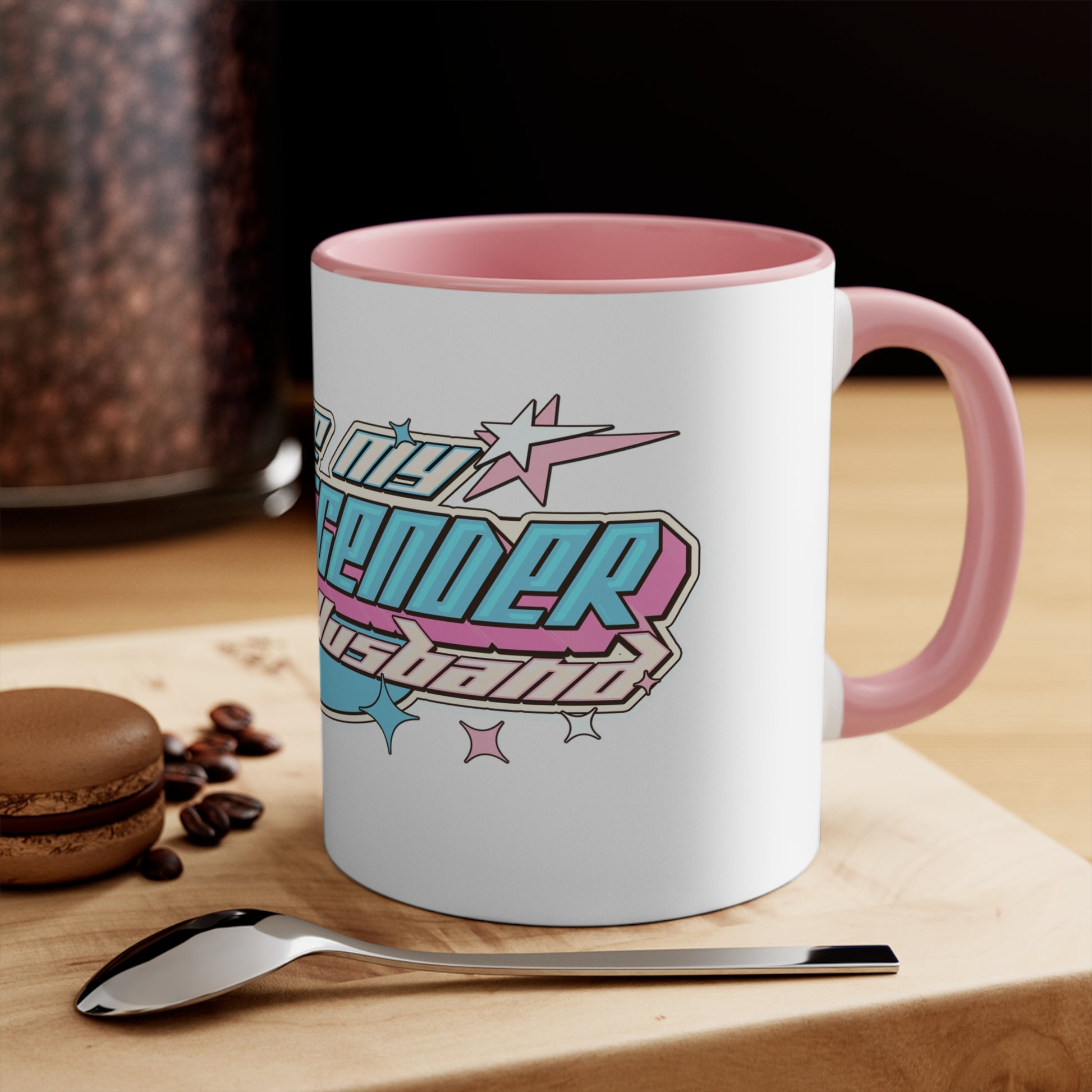 The "I Love My Transgender Husband" original design accent mug by Printify is a white mug with a vibrant interior, featuring bold, retro-styled text. The playful and celebratory design includes stars and geometric shapes in pastel pink, blue, and yellow.