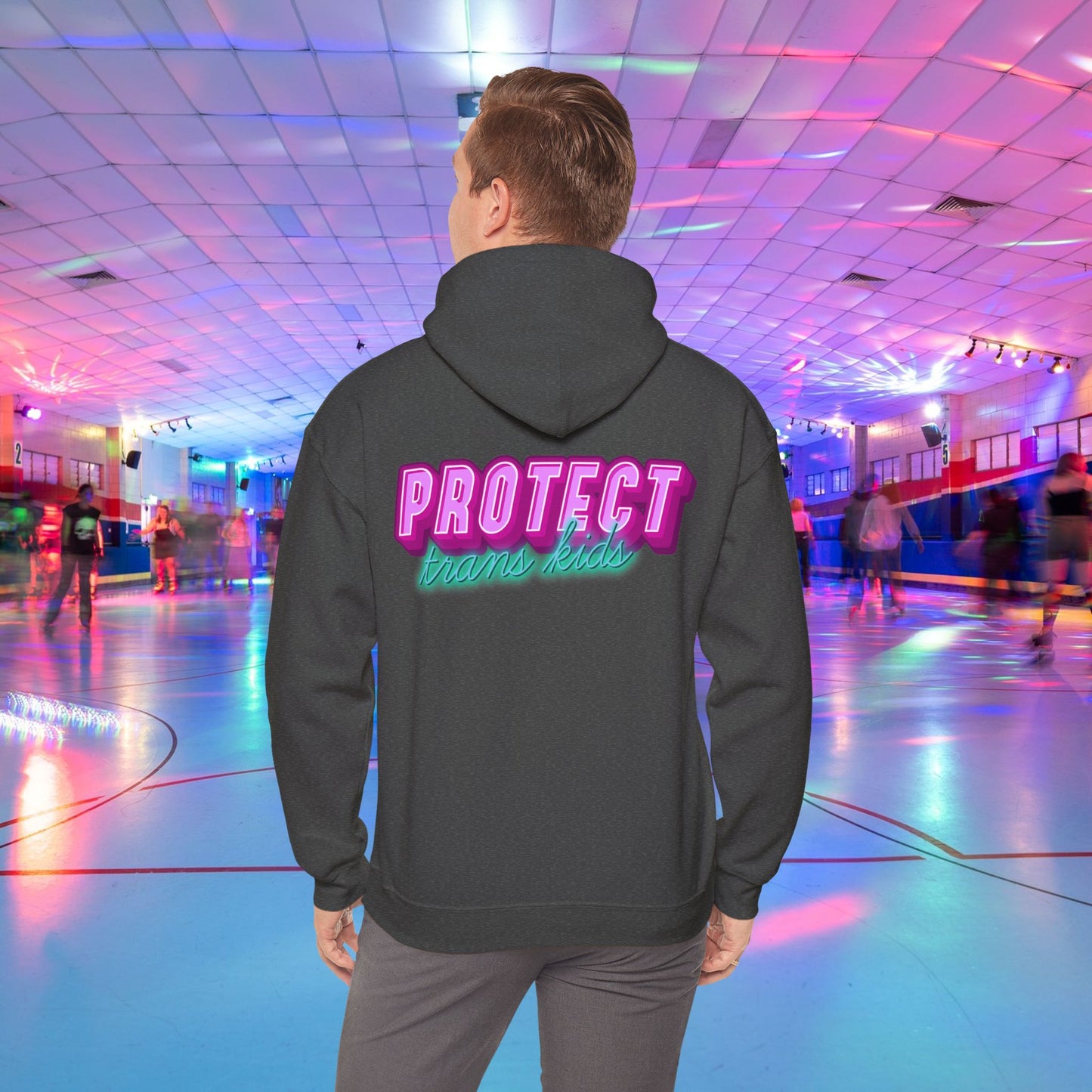 A person in a high-quality Protect Trans Kids Original Hoodie from Printify, crafted from ethically grown cotton, glides effortlessly at a vibrant roller rink illuminated by neon lights. The bold, colorful lettering on their hoodie reads "PROTECT trans kids," while other skaters create a lively, blurred backdrop.