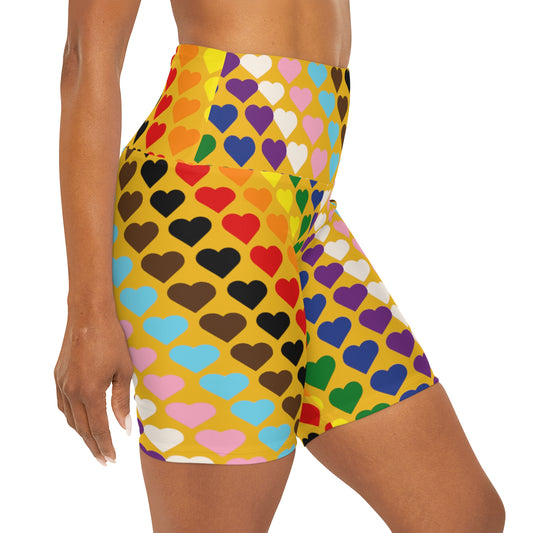 A woman wearing buttery soft, Rainbow Pride Hearts high-waisted yoga shorts in yellow with vibrant, colorful love hearts in red, yellow, blue, green, pink, purple, orange, white, brown and black. The form-fitting shorts feature a playful design. The woman's torso, arm, and upper thigh are visible.