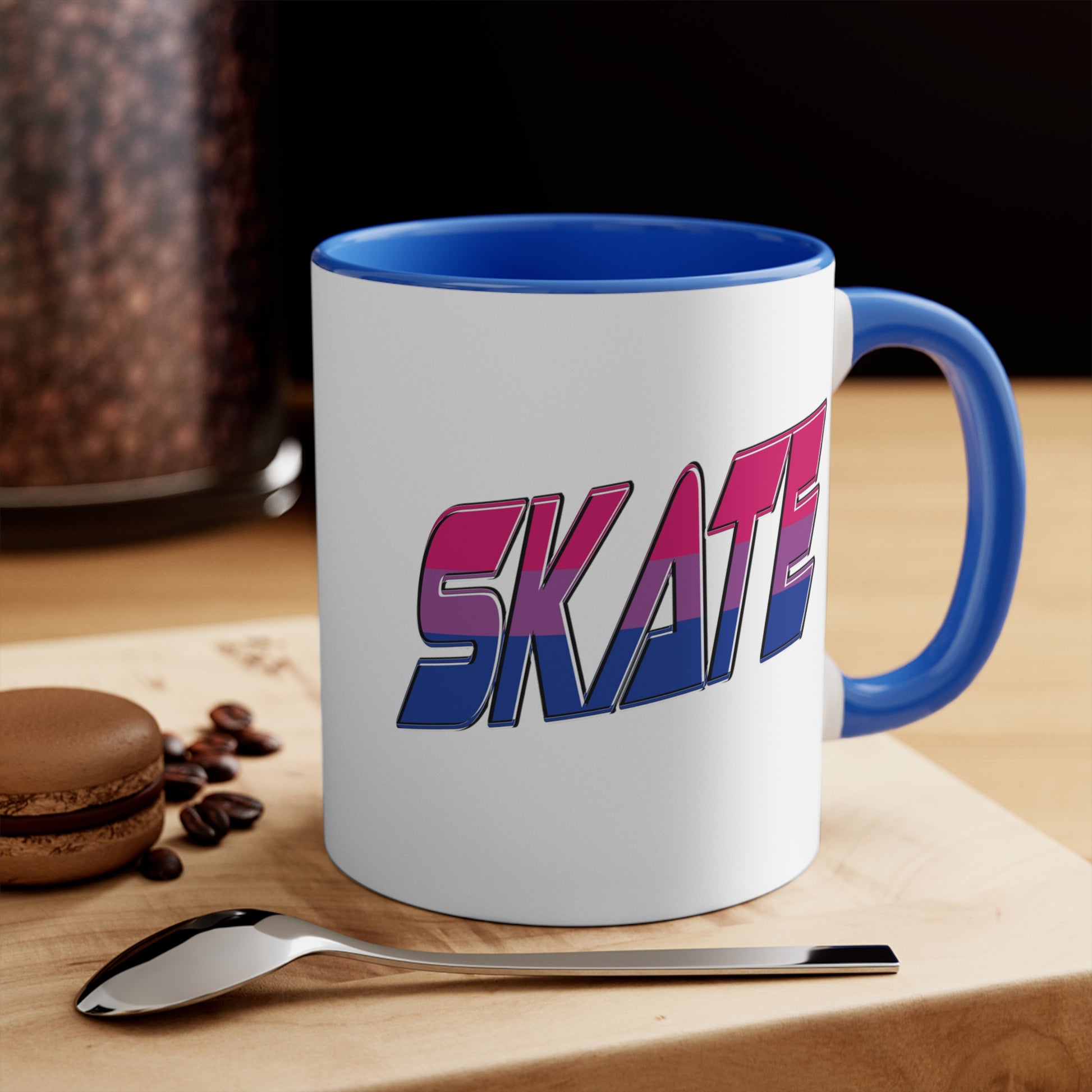 The Printify SKATE bisexual pride flag accent mug features a white base with a blue handle and vibrant interior. It proudly displays the word "SKATE" in bold, stylized gradient lettering, transitioning from pink at the top to blue at the bottom, creating an eye-catching contrast that evokes a sense of movement and energy.