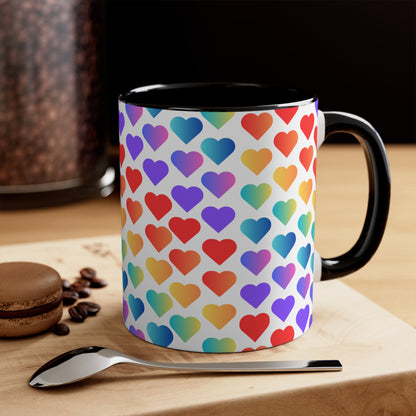 The Rainbow Pride Love Hearts Colorful Accent Mug by Printify is a white mug with a red handle and a colorful interior, adorned with a vibrant pattern of gradient hearts. The hearts transition through various colors, creating an eye-catching color contrast against the white background.