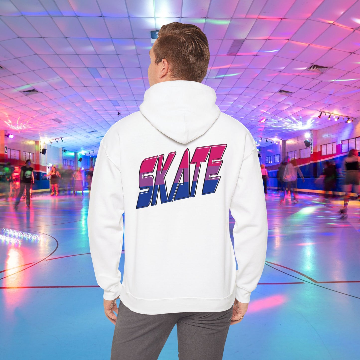 A person in a SKATE Bisexual Pride Hoodie from Printify, with bold and colorful "SKATE" lettering on the back, stands in a brightly lit roller skating rink. The background features skaters gliding on a shiny floor under a ceiling with vibrant, multicolored lights. This unisex heavy blend hooded sweatshirt showcases original designs and is available for Australian shipping.