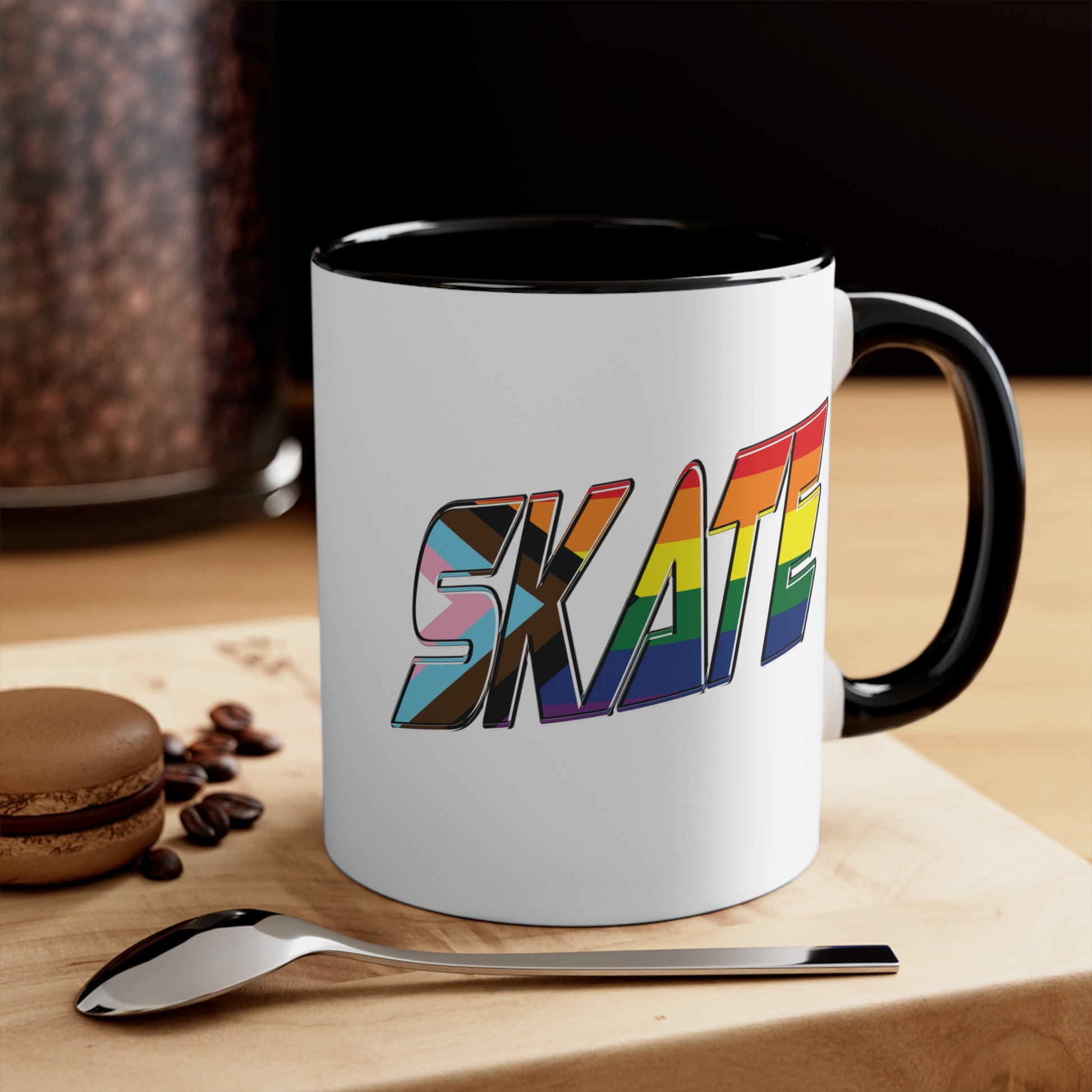 The SKATE progress pride flag accent mug by Printify features a white coffee mug with a red handle and a colorful interior. The front boldly displays the word "SKATE" in rainbow colors, including shades of blue, pink, white, and brown.