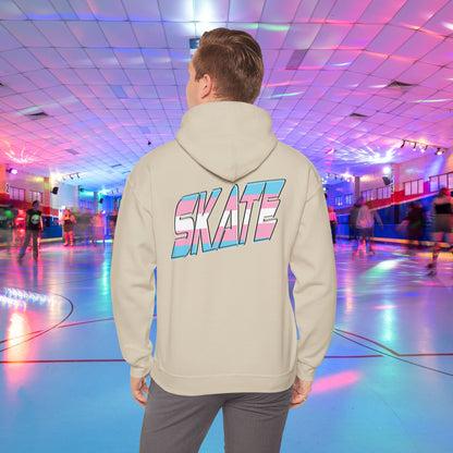 A man with light brown hair, wearing a black hoodie that features "SKATE" in large, colorful letters on the back, stands in a roller skating rink illuminated by vibrant lighting with people skating in the background. The high-quality SKATE Trans Flag Hoodie is made from ethically grown US cotton and is part of Printify's unisex heavy blend collection. Available for Australian shipping.