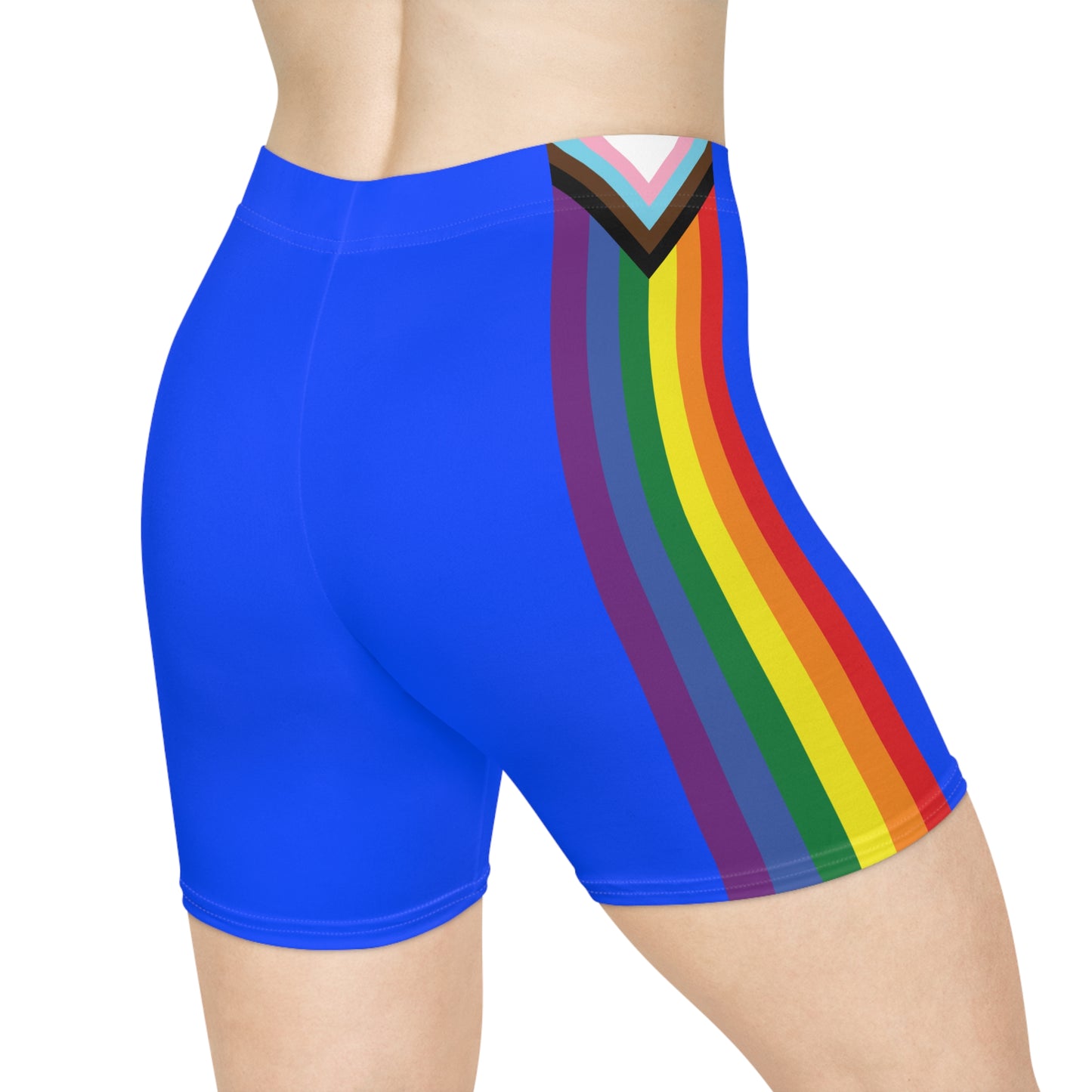 The image showcases a person from the side wearing Printify's Progress Pride Rainbow Flag and Blue Bike Shorts, which feature a vibrant rainbow design incorporating the Pride flag colors, transgender flag hues, and brown and black stripes at the top to symbolize inclusivity.