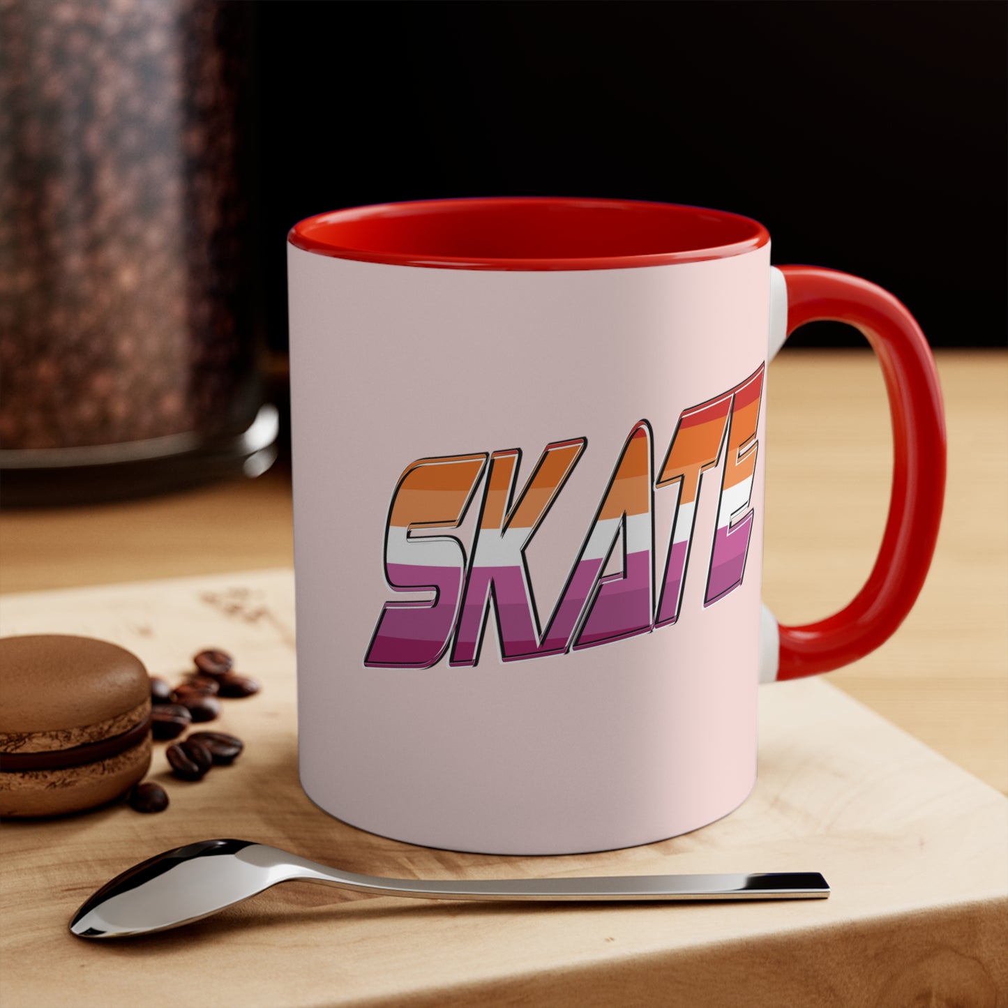 The SKATE lesbian pride flag accent mug by Printify features a bold "SKATE" design in gradient colors of orange, pink, and purple. This eye-catching ceramic mug boasts a light pink handle and interior that beautifully contrast with its pale pink exterior.