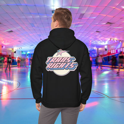 A person wearing a TRANS RIGHTS Hoodie in trans flag colours - Australian Shipping from GAY SKATE stands in a brightly lit roller skating rink, decorated with colorful lights and occupied by people skating in the background.