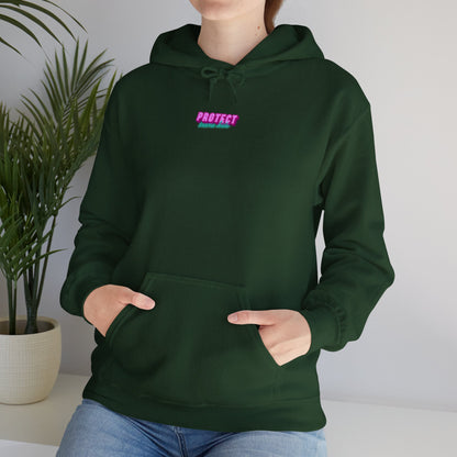 A person wearing the "Protect Trans Kids" hoodie, designed for Australian shipping in dark green with "PROTECT" in pink on the chest, stands with hands tucked into the pocket. Ethically made from cotton, this unisex heavy blend adds a cozy vibe against a backdrop of a potted plant.