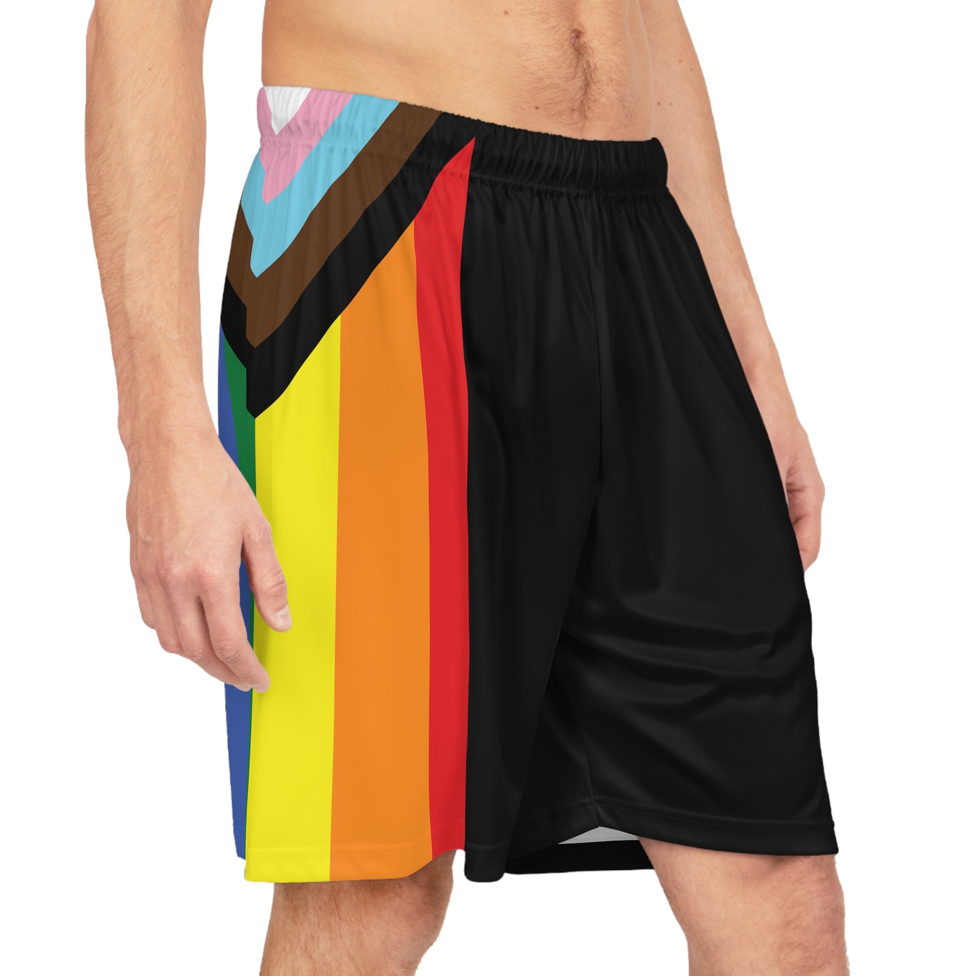 A person is wearing Printify's Progress Pride Rainbow Flag Basketball Shorts made from black, odor-resistant fabric. The shorts feature a vibrant diagonal stripe design in red, orange, yellow, green, blue, brown, black, light blue, pink, and white on the left side. The person's torso is partially visible.