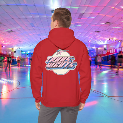 A person wearing a TRANS RIGHTS Hoodie in trans flag colours - Australian Shipping from GAY SKATE stands in a brightly lit roller skating rink, decorated with colorful lights and occupied by people skating in the background.