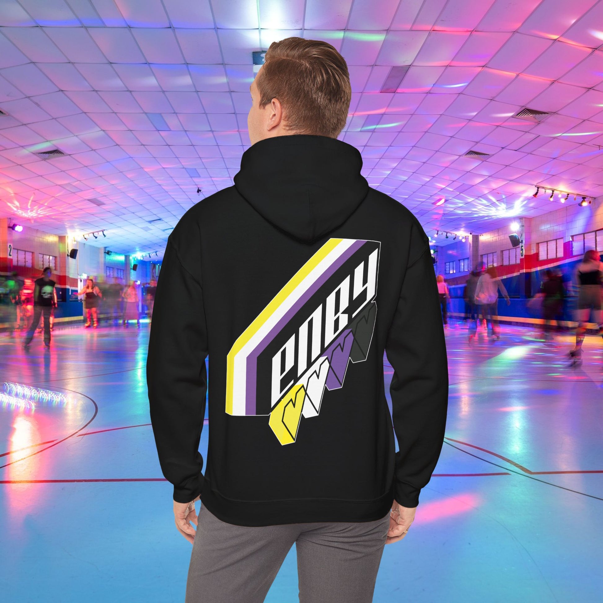 A person wearing the high-quality Printify ENBY Heart Hoodie, a unisex heavy blend hooded sweatshirt, with its colorful geometric nonbinary flag designs on the back, stands in a retro-style roller skating rink. The background features neon lights, blurred skaters, and a vibrant atmosphere.