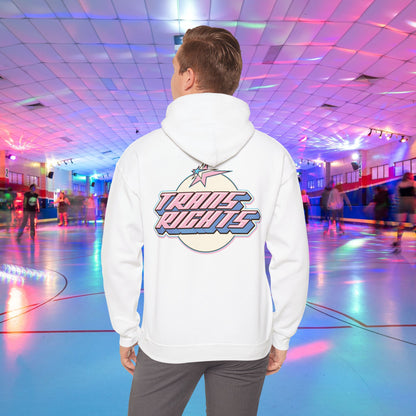 A person wearing a TRANS RIGHTS Hoodie in trans flag colours - Australian Shipping from GAY SKATE stands in a brightly lit roller skating rink, decorated with colorful lights and occupied by people skating in the background.