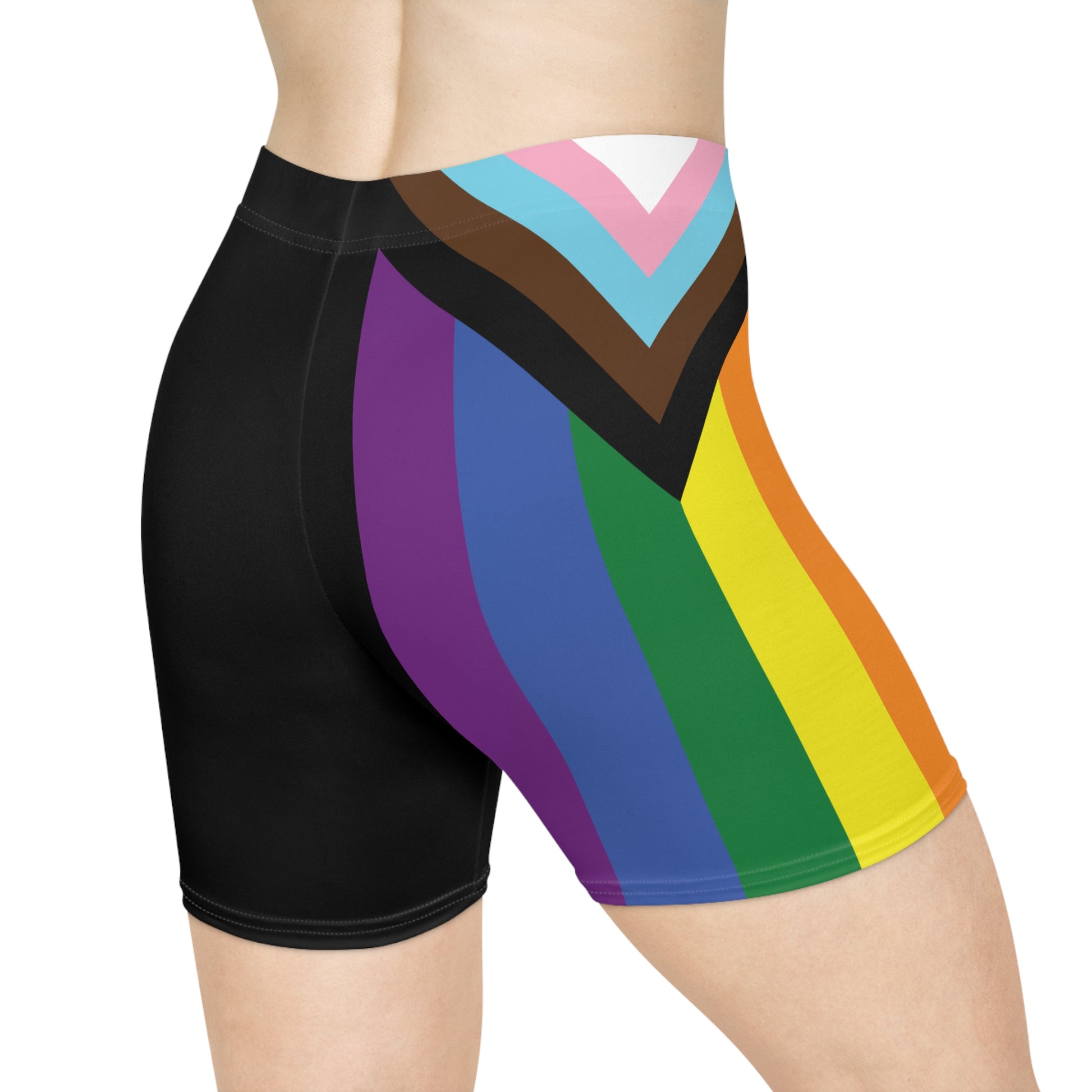 A person is wearing Progress Pride Bike Shorts by Printify, which feature a colorful design with a rainbow pride flag incorporating stripes for people of color and the transgender community. These moisture-wicking shorts fit closely to the body.