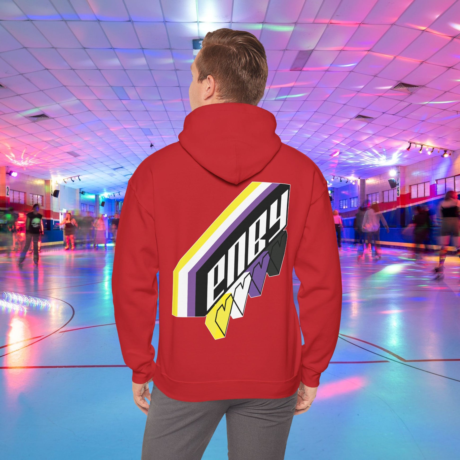 A person wearing the high-quality Printify ENBY Heart Hoodie, a unisex heavy blend hooded sweatshirt, with its colorful geometric nonbinary flag designs on the back, stands in a retro-style roller skating rink. The background features neon lights, blurred skaters, and a vibrant atmosphere.