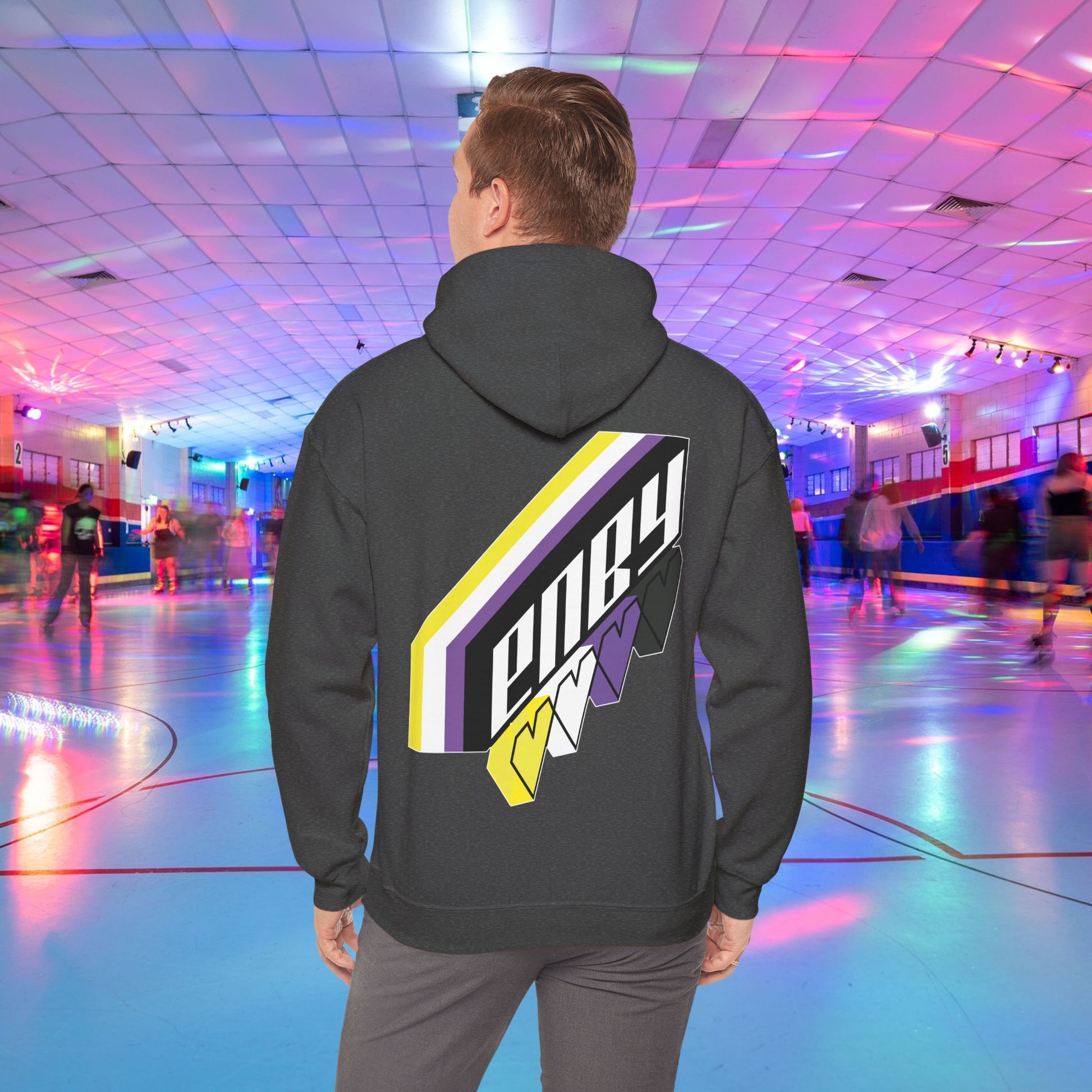 A person wearing the high-quality Printify ENBY Heart Hoodie, a unisex heavy blend hooded sweatshirt, with its colorful geometric nonbinary flag designs on the back, stands in a retro-style roller skating rink. The background features neon lights, blurred skaters, and a vibrant atmosphere.