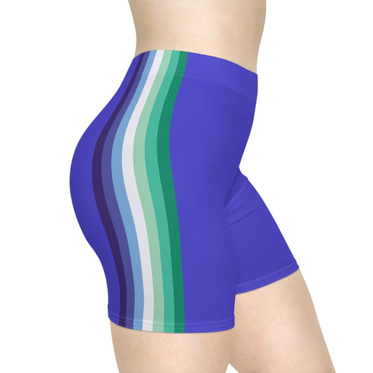 Side view of a person wearing Gay Skate's Gay Men Pride Flag Bike Shorts. The high-waisted, moisture-wicking blue bike shorts feature vertical stripes in various shades of blue and green along the side of dark blue bike pants. Perfect for twinks