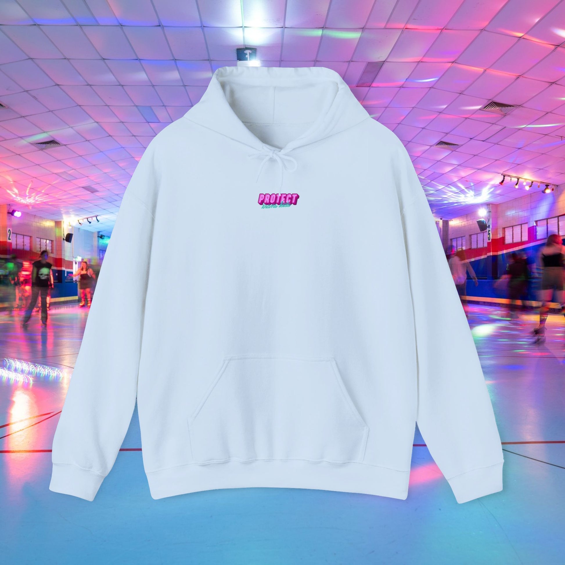 The "Protect Trans Kids Hoodie" is a white unisex heavy blend sweatshirt with "PROTECT" in pink on the chest, made from ethically grown cotton. It stands out against a neon-lit roller rink backdrop, as skate wheel reflections dance across the floor. Available for Australian shipping.