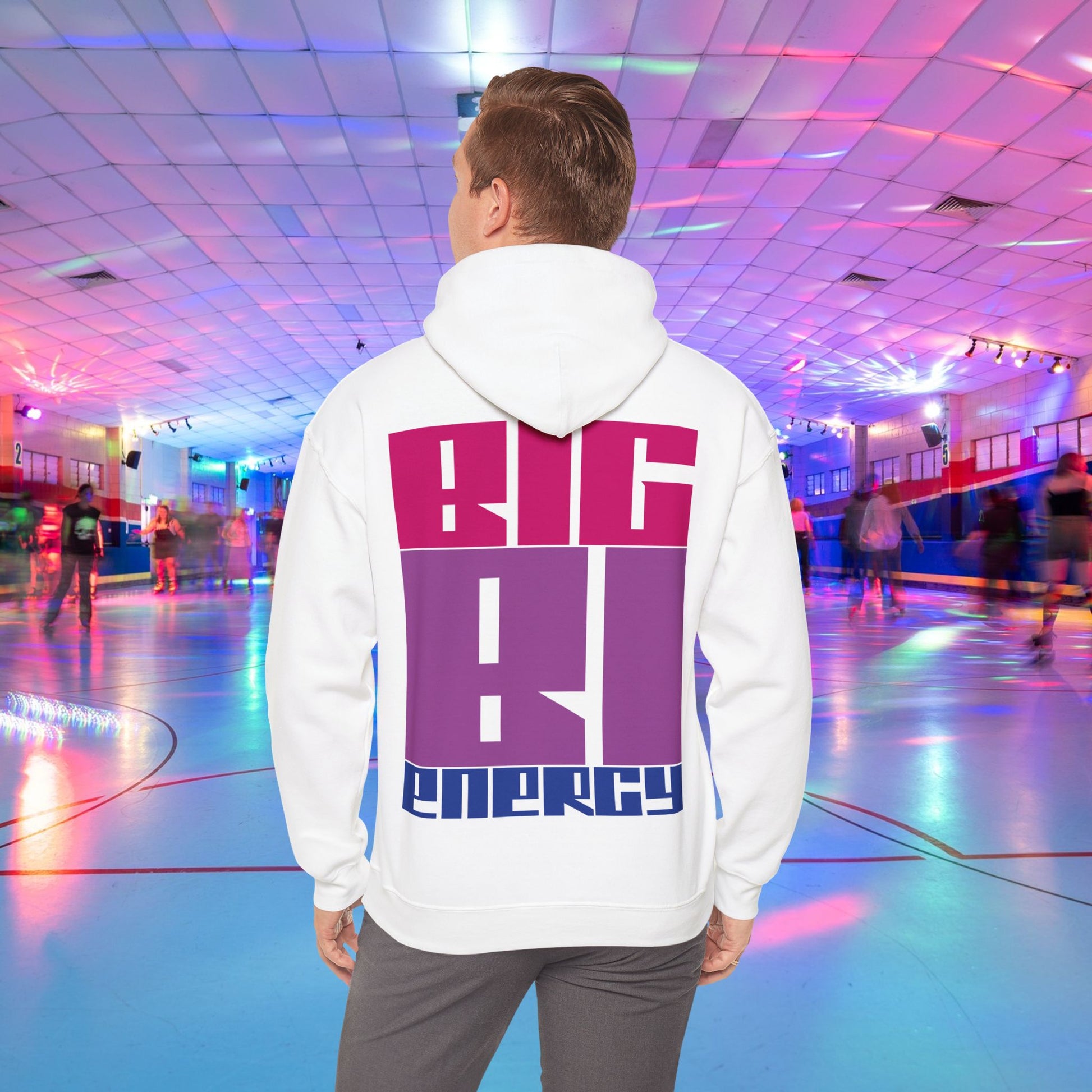 A person with light brown hair is wearing a high-quality BIG BI ENERGY Hoodie from GAY SKATE, featuring bold, Bisexual Pride Flag colour letters on the back. They are standing in a roller skating rink illuminated with vibrant, colorful lights. The cozy feel and warmth of this trans and queer-owned brand is evident.