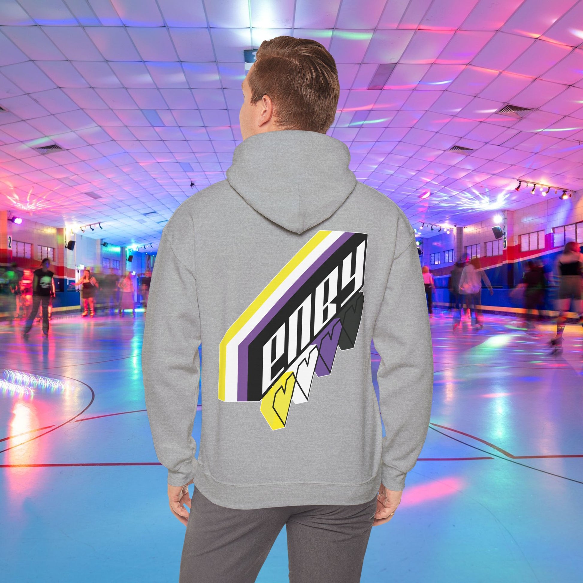 A person wearing the high-quality Printify ENBY Heart Hoodie, a unisex heavy blend hooded sweatshirt, with its colorful geometric nonbinary flag designs on the back, stands in a retro-style roller skating rink. The background features neon lights, blurred skaters, and a vibrant atmosphere.