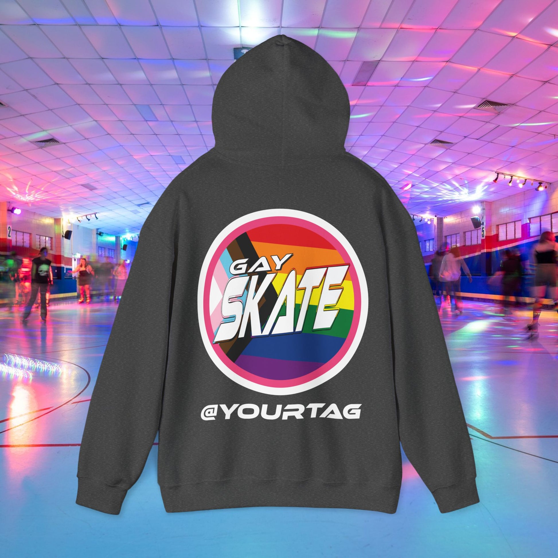 A person facing away from the camera is wearing a Printify Gay Skate Original Hoodie, featuring a large circular logo on the back. The logo has a rainbow background with "GAY SKATE" in bold white letters and "@YOURTAG" at the bottom. The setting appears to be a roller rink, and the unisex heavy blend sweatshirt, available for Australian shipping, is made from ethically grown US cotton.