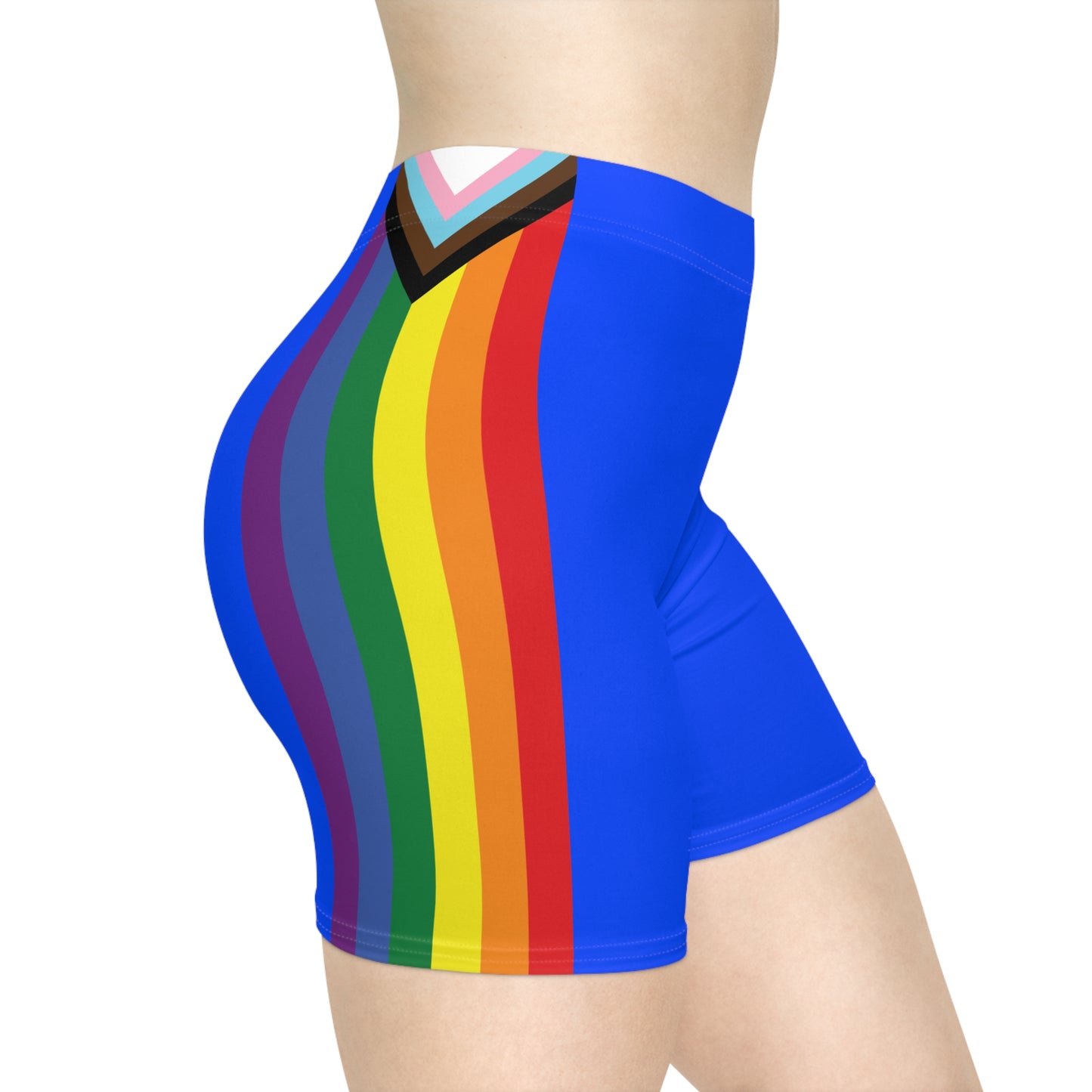 The image showcases a person from the side wearing Printify's Progress Pride Rainbow Flag and Blue Bike Shorts, which feature a vibrant rainbow design incorporating the Pride flag colors, transgender flag hues, and brown and black stripes at the top to symbolize inclusivity.