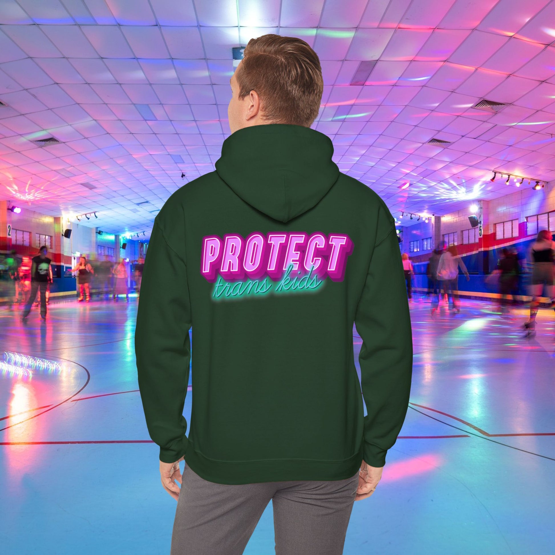 A person is at a roller skating rink, sporting a high-quality Protect Trans Kids Hoodie from Printify, crafted from ethically grown cotton, with "PROTECT trans kids" boldly and colorfully emblazoned on the back. The rink is bathed in vibrant, colorful lights, and other skaters can be seen gliding in the background.