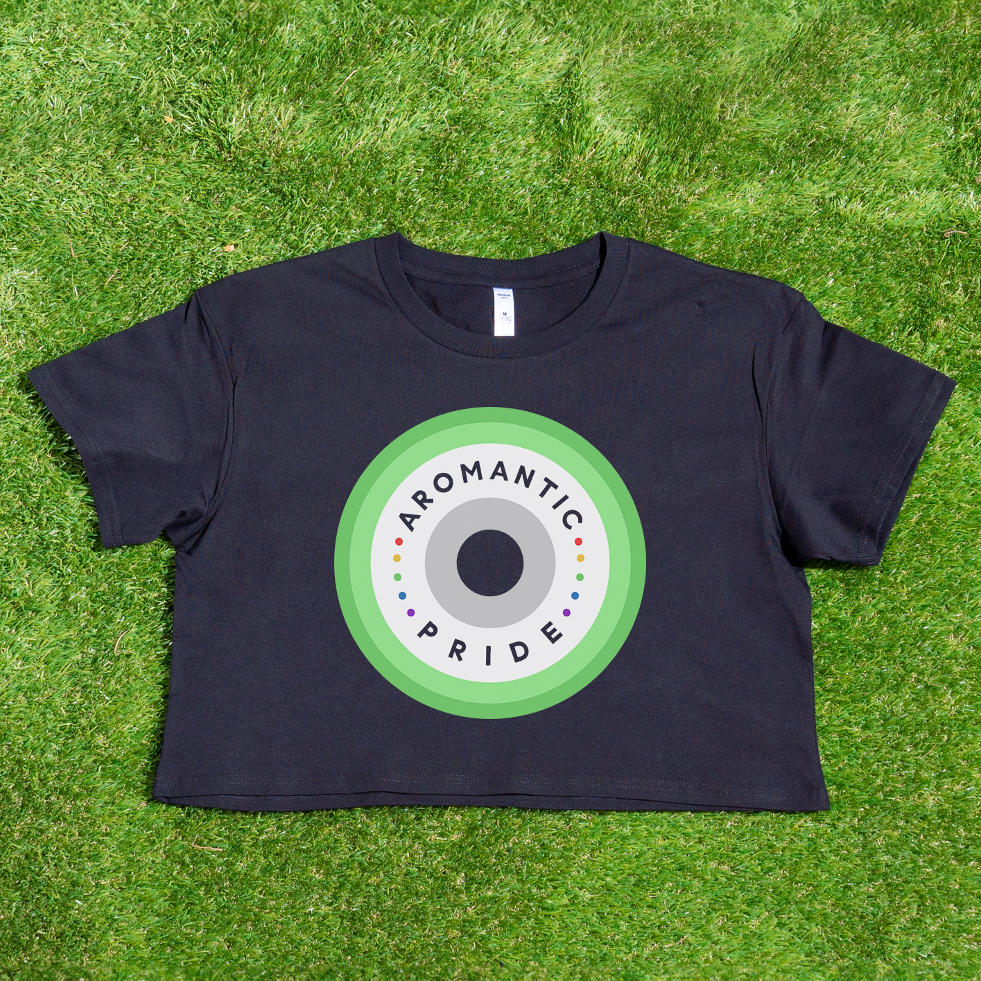 Introducing the Aromantic Pride - Locally Printed Black Crop Tee by Gay Skate, showcasing a circular design in green, white, and gray shades. This proudly queer and trans-owned piece is beautifully highlighted against lush green grass.