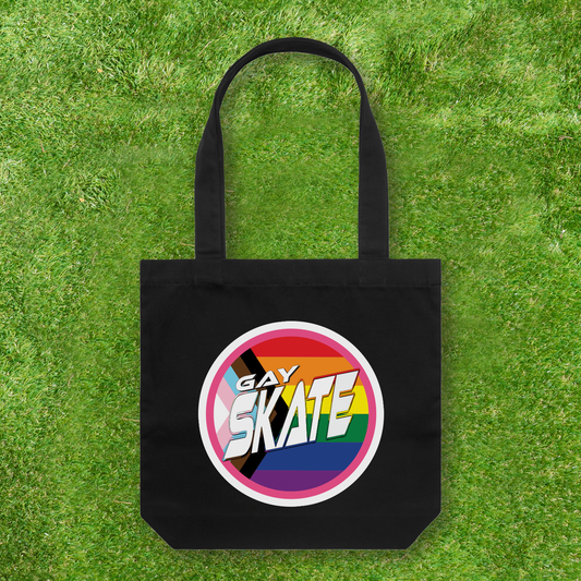 This large black Cotton Canvas Tote Bag from Gay Skate features a vibrant circular "GAY SKATE" logo, representing a queer and trans owned small business. Against a lush green grass background, it serves as both a statement piece and a celebration of bold identity.