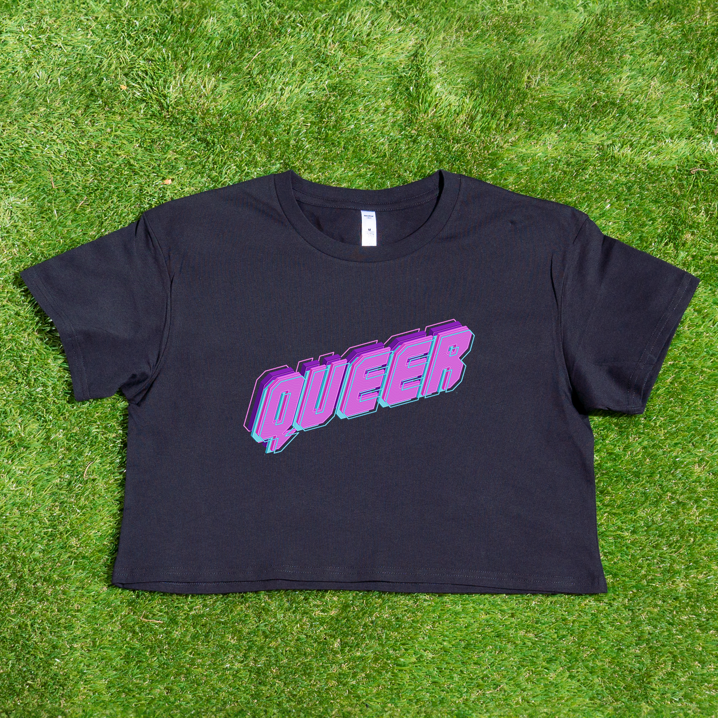 Presenting the "QUEER neon logo - locally printed crop tee" from Gay Skate, a striking black cropped shirt. It features a bold neon-style logo that spells out "QUEER" in eye-catching purple and pink letters, making it the perfect choice for those who embrace the queer skate scene. This standout piece looks particularly vibrant against lush green grass.