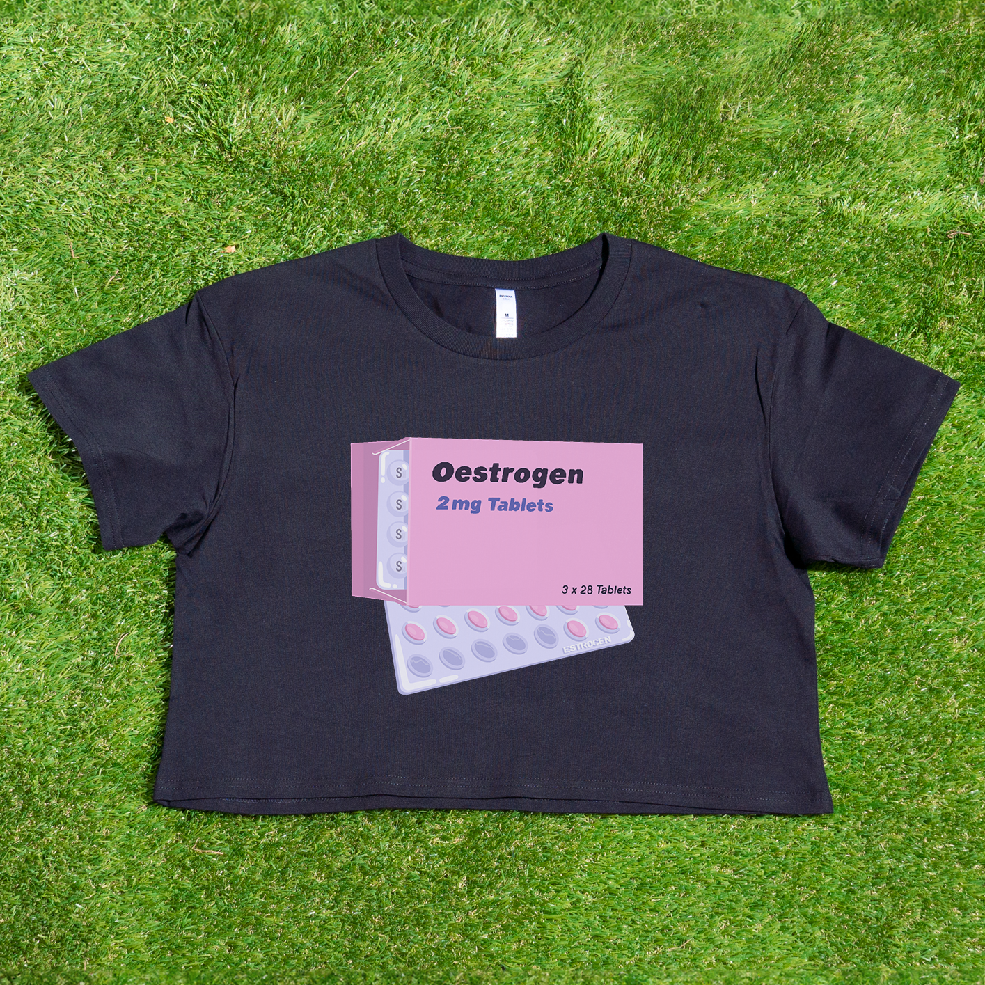 The "Estrogen HRT trans pride" crop tee from Gay Skate is an ideal choice for fans of queer skate streetwear. This black top features a vivid pink graphic depicting an estrogen tablet box and blister packs with the text "Oestrogen 2 mg Tablets." Casually displayed on grass, it makes a striking and bold statement.