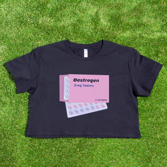 The "Estrogen HRT trans pride" crop tee from Gay Skate is an ideal choice for fans of queer skate streetwear. This black top features a vivid pink graphic depicting an estrogen tablet box and blister packs with the text "Oestrogen 2 mg Tablets." Casually displayed on grass, it makes a striking and bold statement.