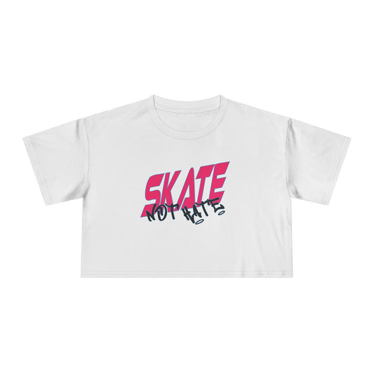 The SKATE NOT HATE original logo crop tee by Gay Skate is a white, short-sleeved shirt featuring the word "SKATE" in bold, pink, slanted capital letters across the chest. The message is accentuated with the word "NOT" in black, distorted text overlaying "SKATE," promoting the message: skate not hate.